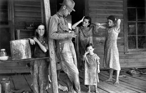 A man named Floyd Burroughs stands with four children on a wooden house porch.