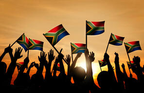 Group of people waving South African flags in back lit.