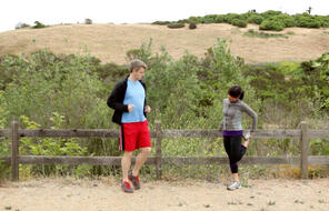 A man and woman warm up for a run on an outdoor trail. 