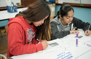 Two middle school students write with pencils on a big paper activity.