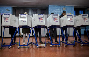 A line of U.S. voters submitting their ballots behind privacy screens.