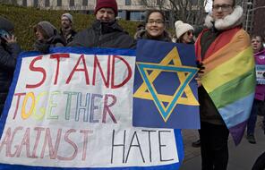 Three people stand together with a sign that has the Star of David on it with the saying "Stand Together Against Hate."