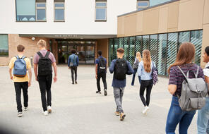 Rear view of high school students walking into college building together