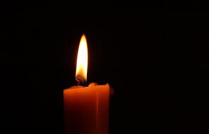A lit candle shines against a dark background