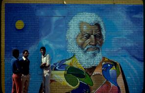 Mural of Fredrick Douglass painted on the side of a brick building with three African American men standing alongside it