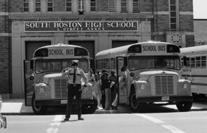 Policemen standing guard while Black students attending South Boston High School climb into buses backed up close to the school's doors