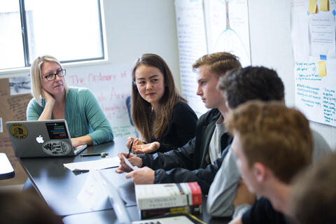 Students and teacher engage in discussion in a classroom. 