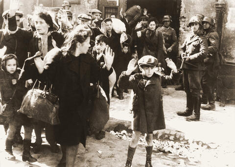 Seven year old boy Tsvi Nussbaum holds his hands up in Warsaw, 1943.