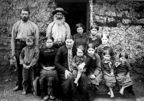A family of four adults and seven children sitting and standing in front of the doorway of a building.