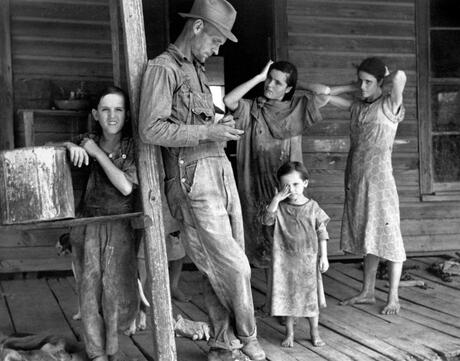 A man named Floyd Burroughs stands with four children on a wooden house porch.