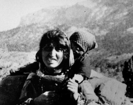 A black and white photo of an Armenian woman carrying her child on her back.