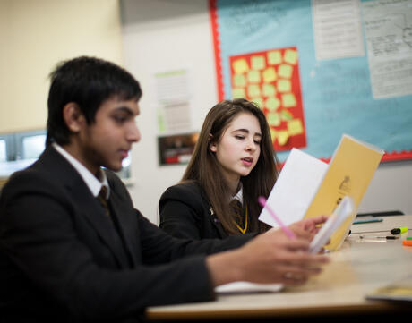 Uniformed high school students read at their desks. 
