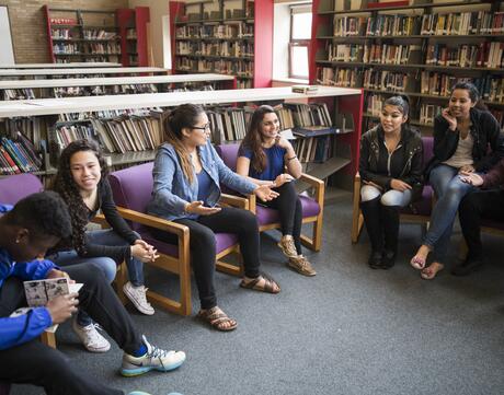 Students sit in a circle in a library and smile and laugh